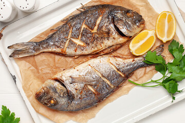 Baked dorado fish with lemon and parsley in a dish on the table. Top View