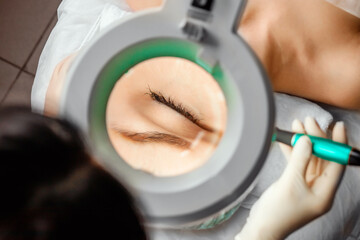 A beautician wearing medical gloves cleans the pores on the face using special equipment while...