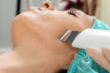 A gloved beautician cleanses the skin on the face using a special gel and equipment. The concept of...
