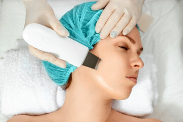 Fototapeta na wymiar A gloved beautician cleanses the skin on the face using a special gel and equipment. The concept of facial hygiene, cosmetic procedures, skin care, skin pore cleansing, hardware cosmetology.