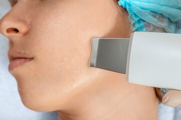 A gloved beautician cleanses the skin on the face using a special gel and equipment. The concept of...
