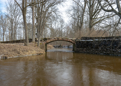 a continuous boulder stone bridge with a brick used for masonry, early spring, bare trees, snow plan on the ground, Stone arch bridge over the river Kuja, Madona, Latvia