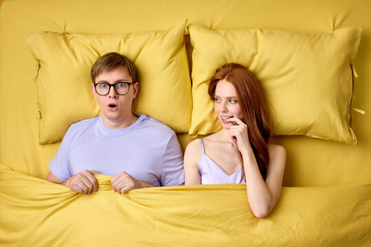 Embarrassed and shy man in shock lying on bed with experienced excited female before his first intimacy in bed