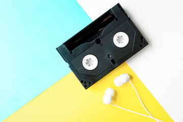 Audio cassette on a colored background with headphones. Equipment and items from different time periods. Obsolete and new things. Nostalgia for the old days.