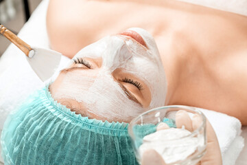 A beautician applies a mask to the face in a beauty salon. The concept of facial hygiene, cosmetic...