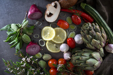 Fresh green fruits and vegetables on a table. Top view photo of green apples, artichoke flowers, zucchini, almonds, avocado and herbs. Healthy eating concept. Gray background with copy space.