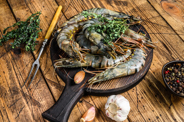 Raw black tiger shrimps prawns on a cutting board with herbs.  wooden background. Top view