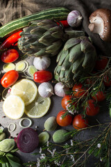 Vegetarian meal ingredients on a table. Top view photo of fresh seasonal vegetables. Artichoke, pepper, mushroom. cherry tomatoes, red onion, zucchini, spices and herbs on gray background. 