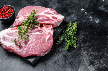 Raw pork meat steaks on a marble board. Black background. Top view. Copy space