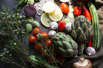 Vegetarian meal ingredients on a table. Top view photo of fresh seasonal vegetables. Artichoke, pepper, mushroom. cherry tomatoes, red onion, zucchini, spices and herbs on gray background. 