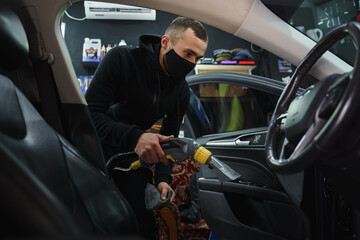 Man cleans car with a vacuum cleaner and disinfects