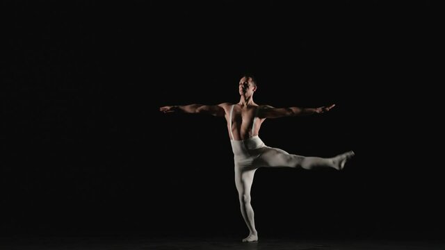 Male ballet dancer performs ballet dance on a black background. He spins on his leg. Slow motion