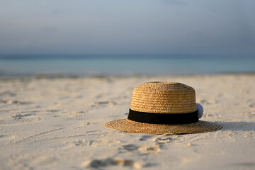Women's straw hat with black ribbon is lying on the white sand on the beach,blue sea and blue sky in the background, copy the space for text.Sun hat on the sand on a sunny day.Vacation, Summer concept
