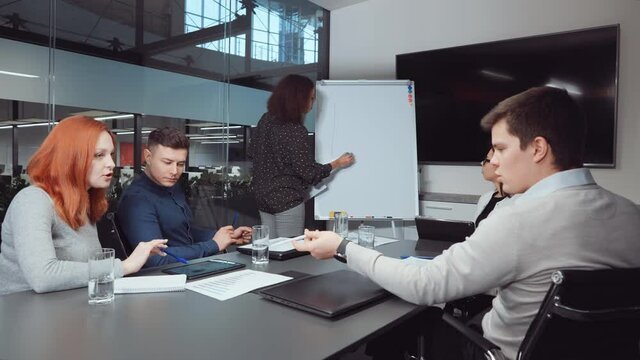 Group of managers sitting in meeting room and having discussion, Black woman standing by flipchart and drawing growth graph. Multiethnic startup team planning strategy and brainstorming