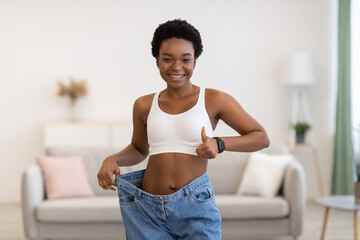 Fototapeta na wymiar Cheerful Black Woman Wearing Huge Jeans After Slimming At Home