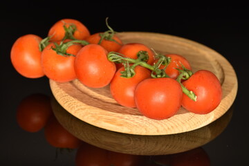 A group of several ripe, bright red, organic, delicious cocktail tomatoes, close-up, on a round bamboo tray, on a black background.