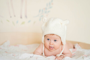 A baby wearing a bear hat lies on its stomach