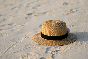 Fototapeta na wymiar Women's straw hat with black ribbon is lying on the white sand on the beach. Sun hat on the sand on a sunny day. The concept of rest and travel on the sea. Beautiful white beach sand with straw hat