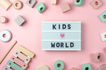 Kids world - text on display lightbox and toys for little children on pink background. Flat lay. Сolored pastel wooden toys, xylophone.