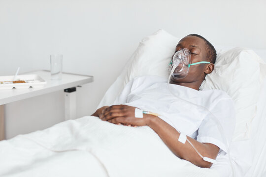 Portrait of African-American man in hospital bed with oxygen mask and iv drip, copy space