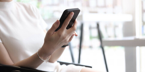 Close up of female hands using modern smart phone while working at office with computer, businesswoman typing text message on her cellphone.