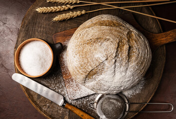 A round loaf of freshly baked sourdough bread flavored with hemp flour, with a knife on a cutting board. Craft bread with seeds on a dark table. Country style sourdough bread