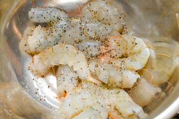 Fresh shrimp marinated with salt and pepper in a silver marinated bowl.