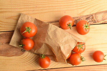 Ripe organic, red tomatoes with a paper bag, close-up, on a wooden table.