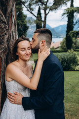 Walk of the bride and groom in the summer park. Newlyweds in seclusion. He and she are by the big tree.