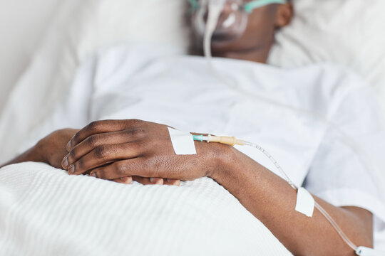 Close up of unrecognizable African-American man lying in white hospital bed with focus on iv drip catheter in hand, copy space