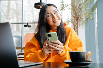 Smiling asian woman using mobile phone while working with laptop