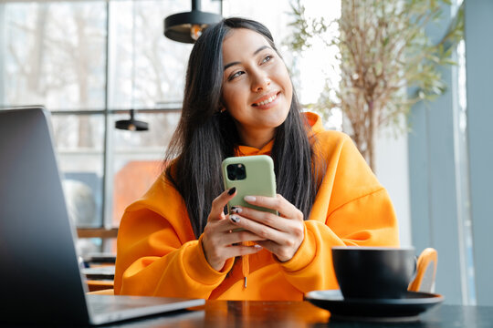 Smiling asian woman using mobile phone while working with laptop