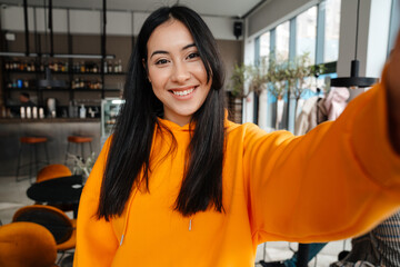 Young asian woman smiling while taking selfie photo in cafe