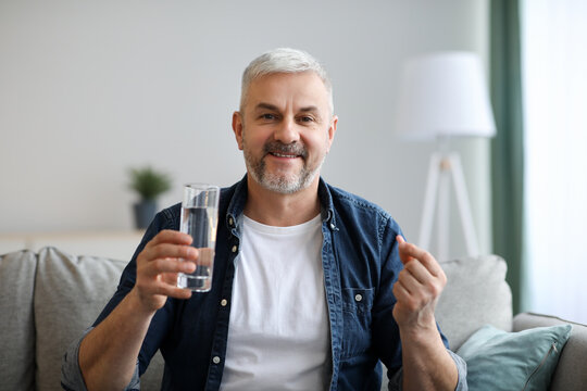 Smiling senior man with glass of water taking medicine