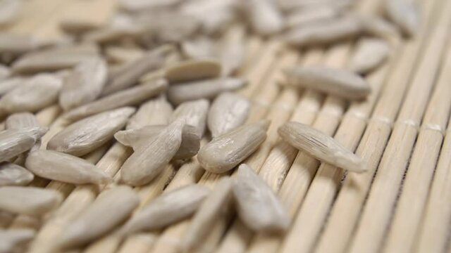 Falling peeled uncooked sunflower kernels in slow motion onto the bamboo mat surface. Raw seeds. Macro. Dolly Shot