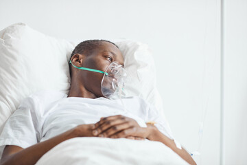 Portrait of young African-American man in hospital bed with oxygen mask , copy space