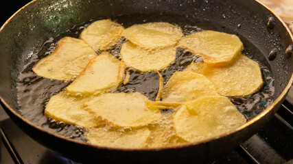 Close view of a bunch of potato slices being fried in  a pan