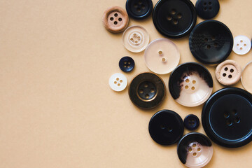 Black round buttons of different sizes on a beige background, top view. Needlework and sewing concept. Copy space.