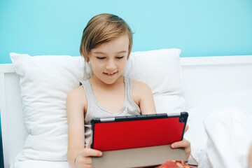 Cute child using digital gadget in bed before going to sleep. Boy watches video and plays games on tablet.