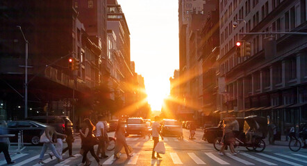 Busy intersection with crowds of people and cars on Fifth Avenue in Midtown Manhattan with rays of sunlight shining in the background of New York City