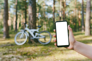Mockup of a smartphone in a girl's hand. Against the background of a bicycle in the forest.
