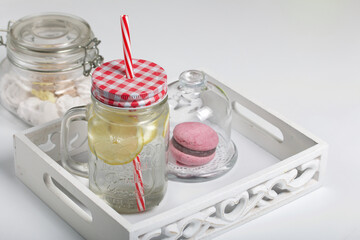 Refreshing drink with lemon. In a glass jar with a lid and a straw. Nearby dessert.