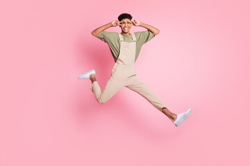 Fototapeta na wymiar Full length body size photo of guy in overall jumping showing v-signs gesture with both hands isolated on pastel pink color background