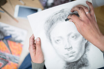 Top view of a close up of the hands of a person drawing a portrait in charcoal on a canvas. Concept of painting classes. Selective focus. Space for text.
