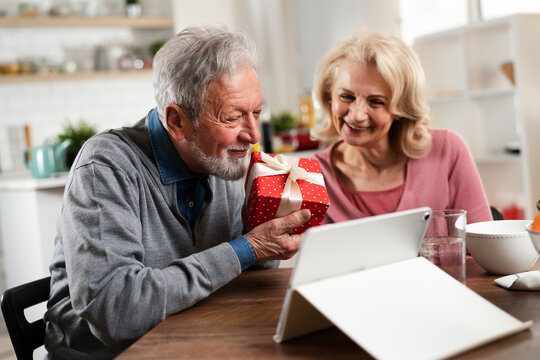 Senior couple having video call. Happy husband giving his wife a gift - Powered by Adobe
