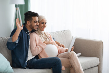 Obraz premium Joyful Expectant Muslim Spouses Making Video Call With Digital Tablet At Home