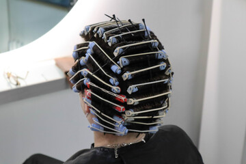 young woman with hair curlers on head, getting perm from hairdresser - obrazy, fototapety, plakaty