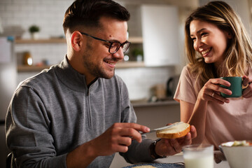 Beautiful woman enjoying in breakfast with her boyfriend. Happy young couple drinking coffee and eating sandwich at home.