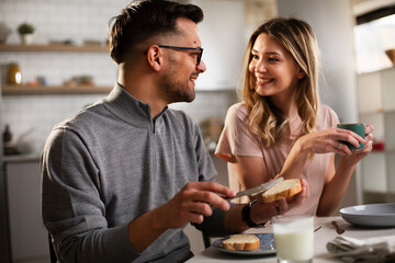 Beautiful woman enjoying in breakfast with her boyfriend. Happy young couple drinking coffee and eating sandwich at home.