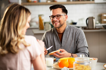 Fototapeta premium Beautiful woman enjoying in breakfast with her boyfriend. Happy young couple drinking coffee and eating sandwich at home.